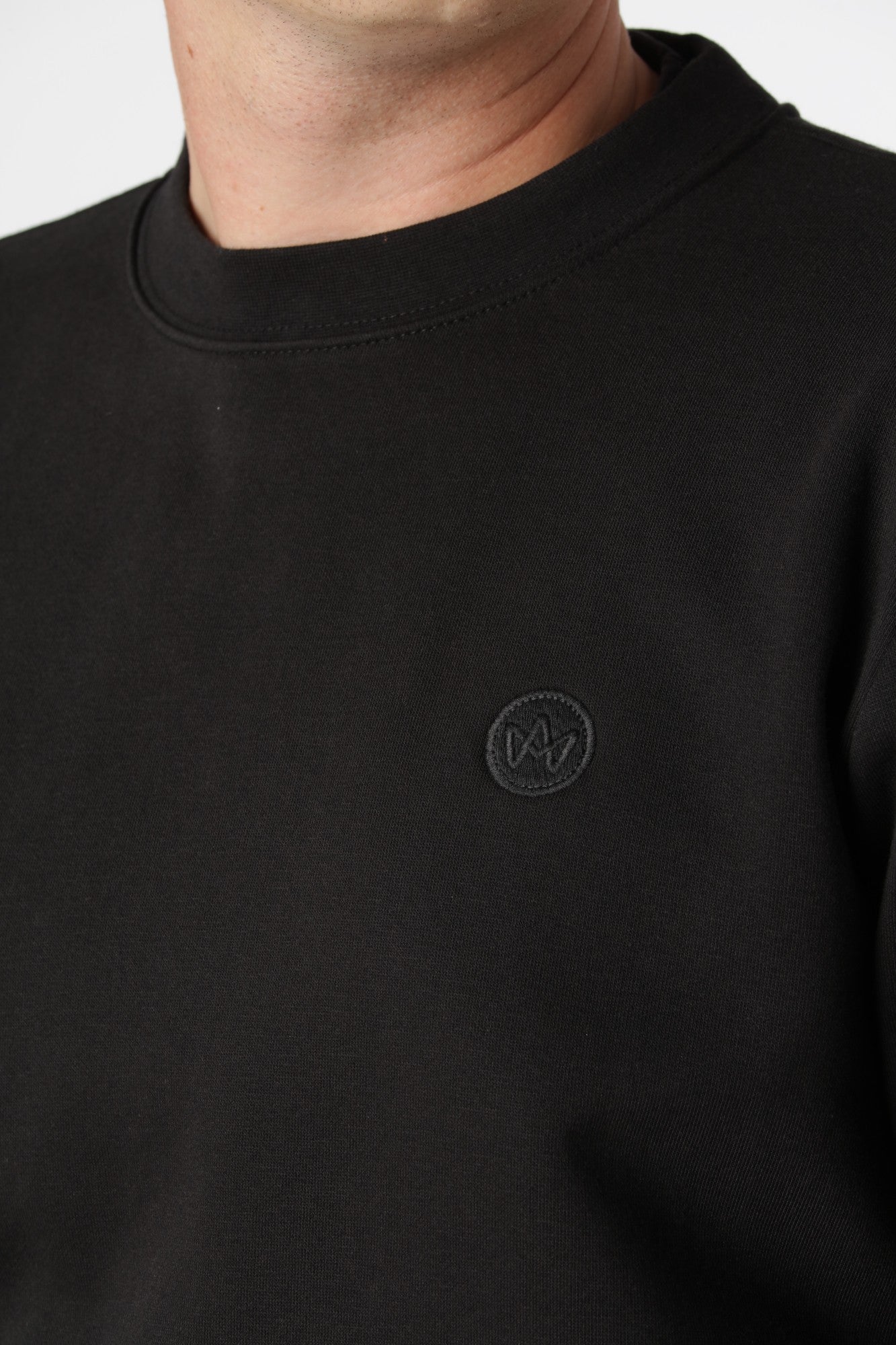 Sort Kronstadt sweatshirt med farverigt broderi på brystet, som bryder den enkle sorte overflade.