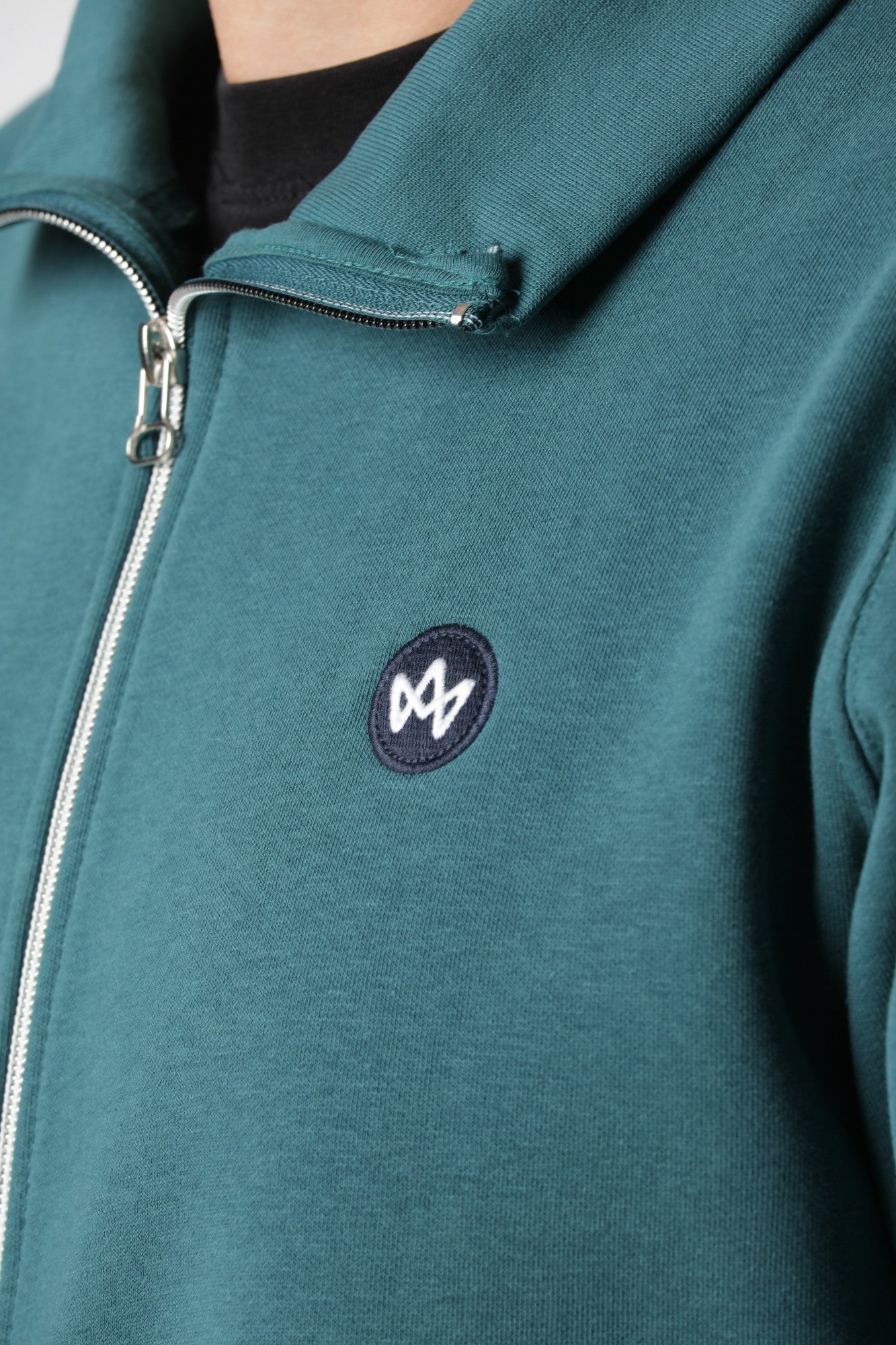 Kronstadt Zip-up i farven Mediterranea med diskret brystbroderi og underspillet blågrønt look